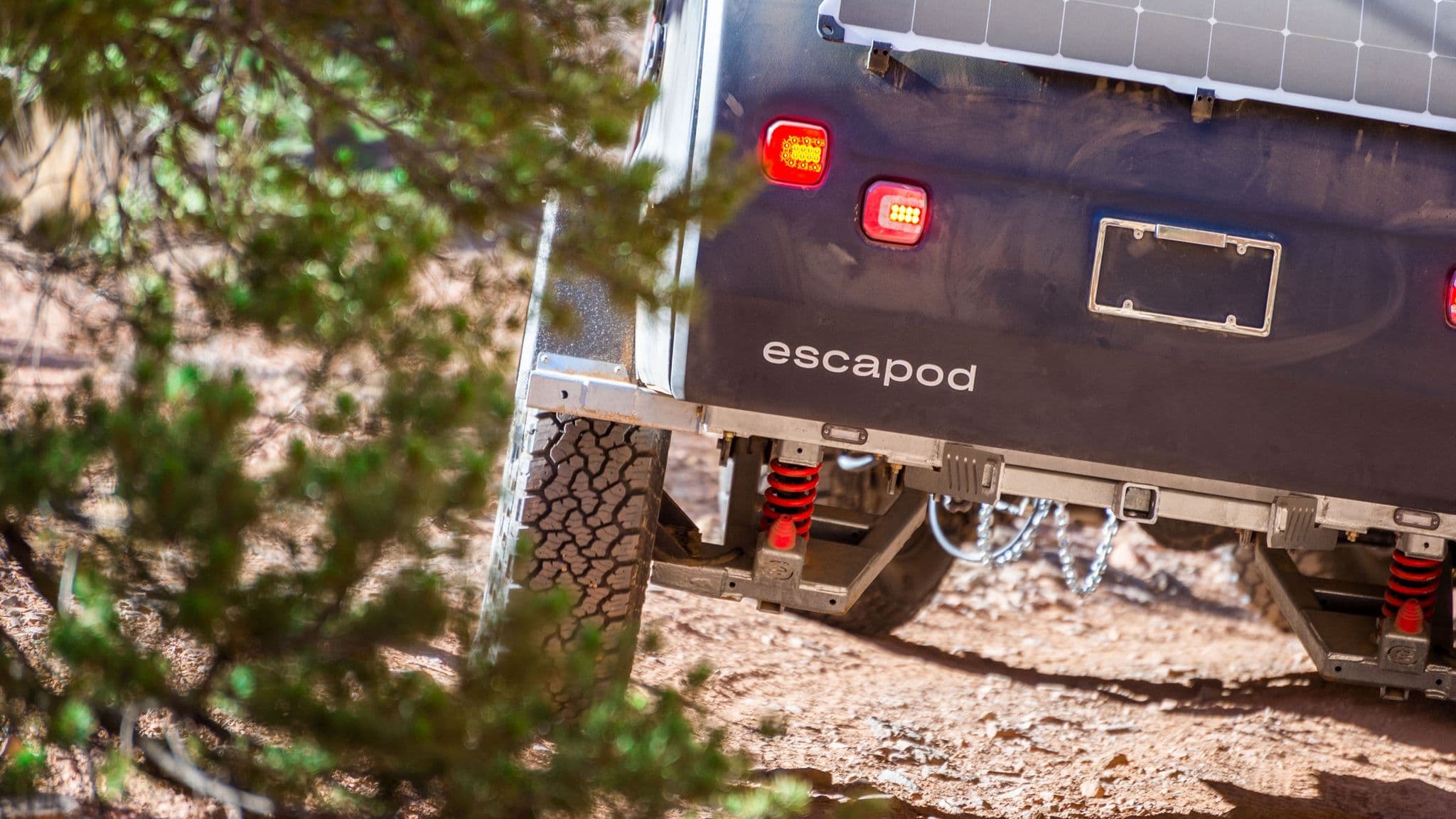 Close-up of Escapod trailer's off-road suspension system with red coil springs, rugged tires, and solar panel, built for extreme terrain.
